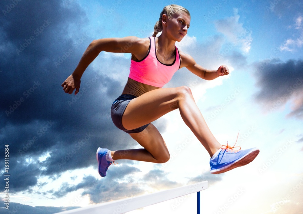 Athlete jumping over a hurdle against sky in background Athlete jumping over a hurdle against sky in background