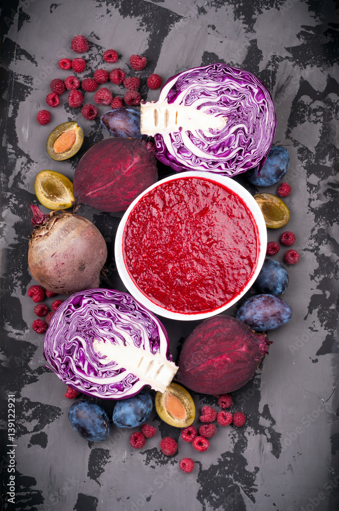Smoothies bowl with purple fruit and vegetables on dark background. Healthy eating and diet concept. Top view