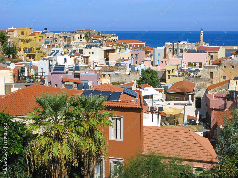 Panorama of Chania old town top view. Old houses with red roofs, Venetian lighthouse. Sailboats in sea and clear sky.