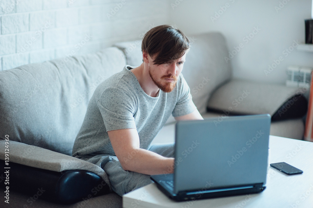 A bearded man with a laptop sitting on the sofa at home
