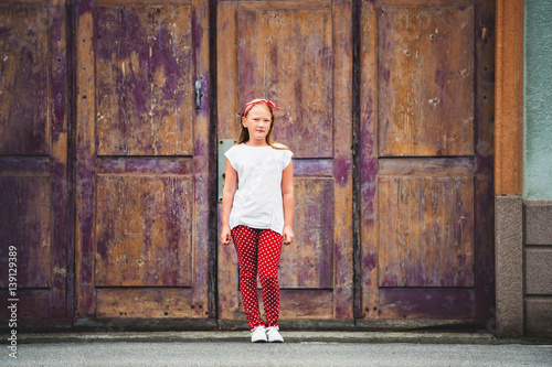 Outdoor fashion portrait of 8-9 year old girl walking down the street, wearing polkadot trousers and white tee shirt, toned image