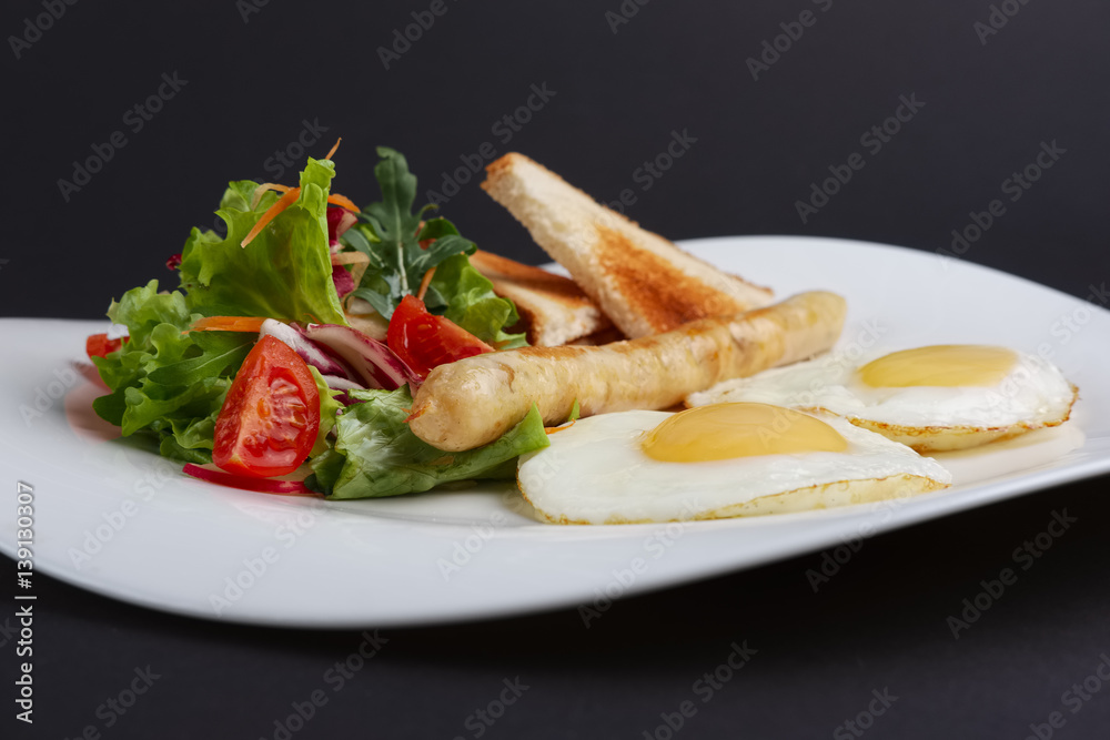 Closeup view of fried eggs with homemade sausage, toasts and fresh tomato and salad. Closeup view of fried eggs with homemade sausage, toasts and fresh tomato and salad.