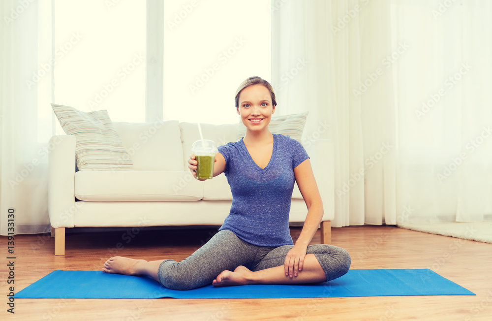 happy woman with smoothie sitting on mat at home
