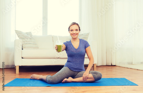 happy woman with smoothie sitting on mat at home