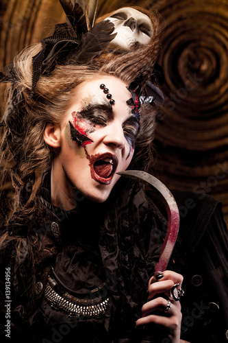 Young  witch hloding sickle. Bright make up, skull, smoke-  halloween theme. photo