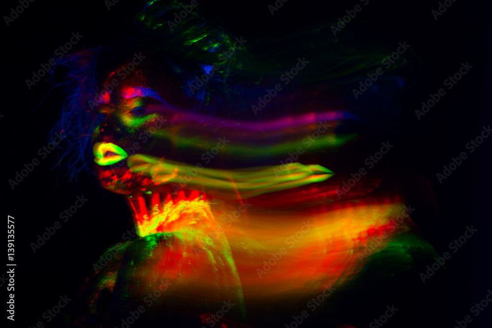 Fototapeta premium Beautiful extraterrestrial model woman with blue heair and green lips in neon light. It is portrait of beautiful model with fluorescent make-up, Art design of female posing in UV with colorful make up