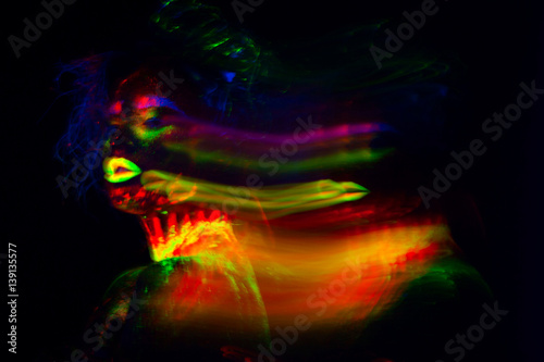 Beautiful extraterrestrial model woman with blue heair and green lips in neon light. It is portrait of beautiful model with fluorescent make-up, Art design of female posing in UV with colorful make up