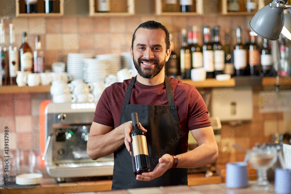 happy man or waiter with bottle of red wine at bar