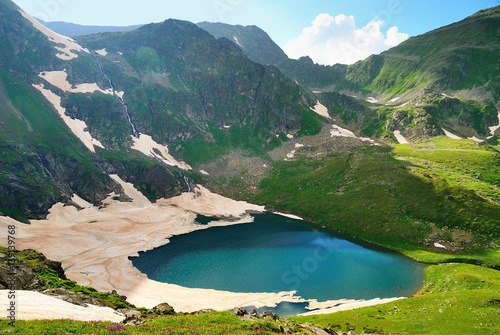Mountain Lake with clean water and ice in the Caucasus summer. Blue sky with white clouds.