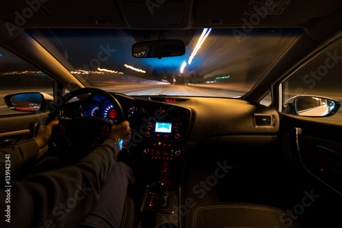 hands on the wheel a car moves at fast speed at the night. Blured road with lights with car on high speed. Car speed night drive on the road in city © narozhnii