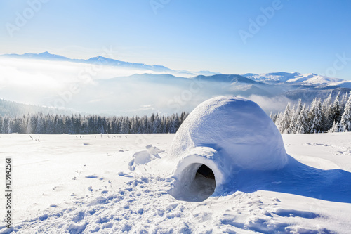Big round igloo stands on mountains covered with snow.