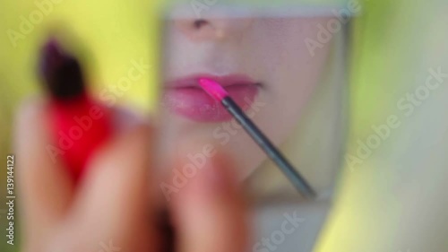 Young woman doing makeup with lipstick looking to handheld mirror photo