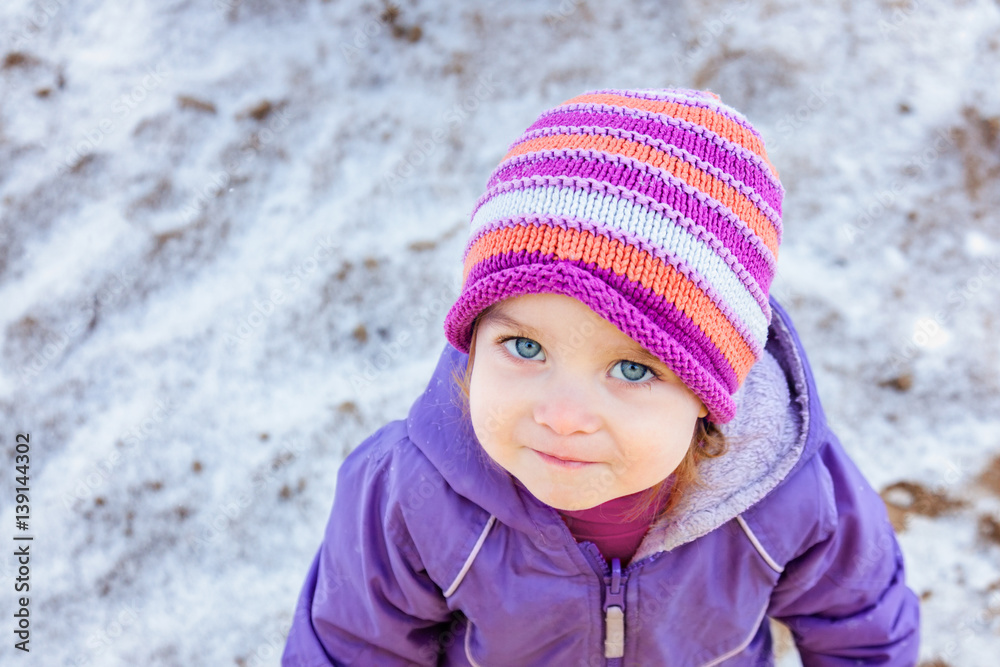 Portrait of little girl one year old looking straight to the camera in winter park. Snowy weather.