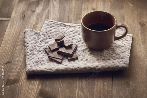 brown cup with black coffee saucer US, crushed chocolate, a spoon colored embroidered stitches gray linen towels, tablecloths on the old brown wooden background close plan