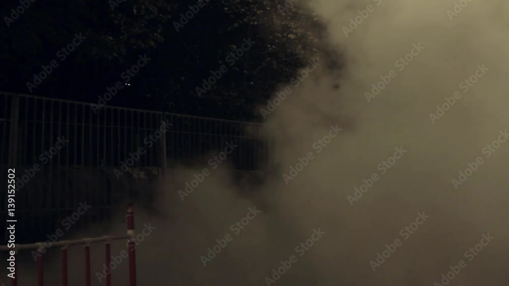 Girl in coat standing on night city street, steam cloud quickly spread around