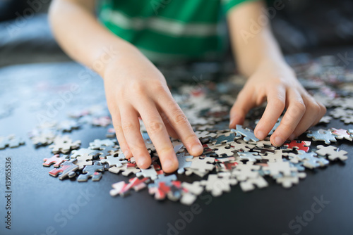 Hands of a child doing a puzzle at table
