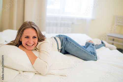 Smiling thoughtful pretty woman lying in bed at home
