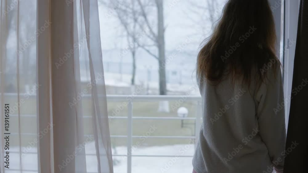 Attractive young woman opens curtains and is opening the door to her balcony Attractive young woman opens curtains and is opening the door to her balcony