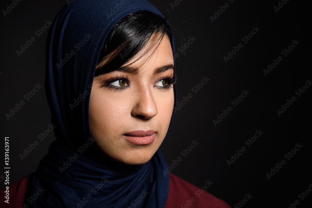 Portrait of a beautiful Muslim woman dressed in hijab on a black background in photo studio.