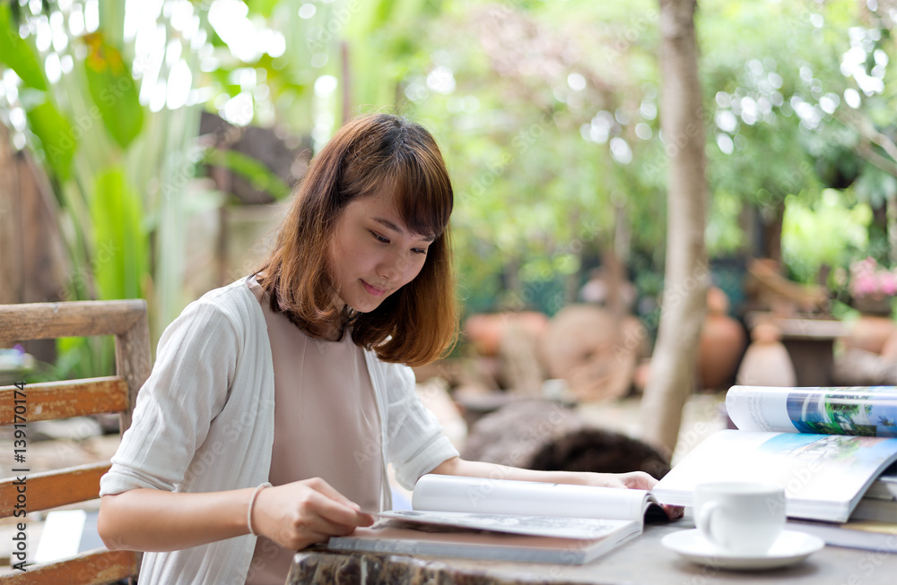 Fototapeta premium Young woman reading magazine with cofee break in garden on summer day, select focus