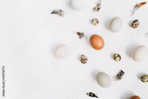 White and brown Easter eggs, quail eggs and feathers on white background. Flat lay, top view. Traditional spring concept.