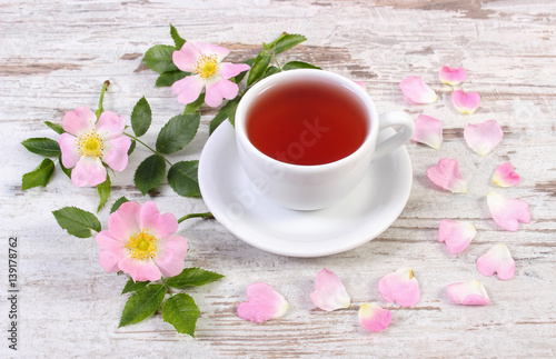 Cup of tea and wild rose flower on old rustic wooden background