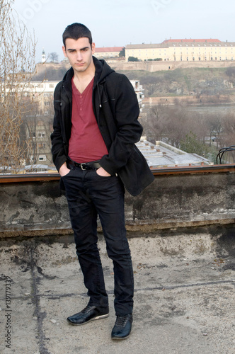 Photographing Danila Mazić in a tight red shirt covered with unbuttoned a black coat and black pants a background Petrovaradin fortress and the Danube River, Novi Sad, Serbia photo