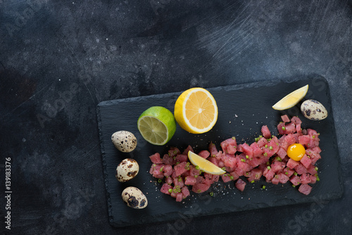 Stone slate with tuna tartare on a dark scratched background, above view, copy space