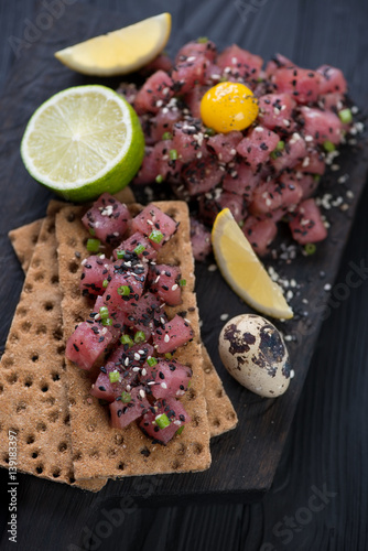 Tuna tartar with black and white sesame, quail egg yolk and slices of bread, close-up