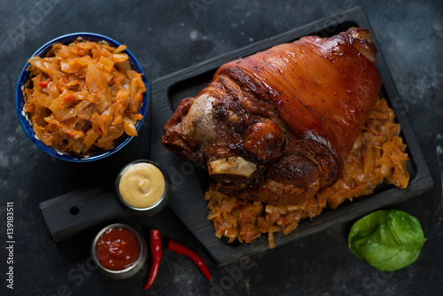 Black wooden serving board with whole baked pork knuckle and braised cabbage, top view