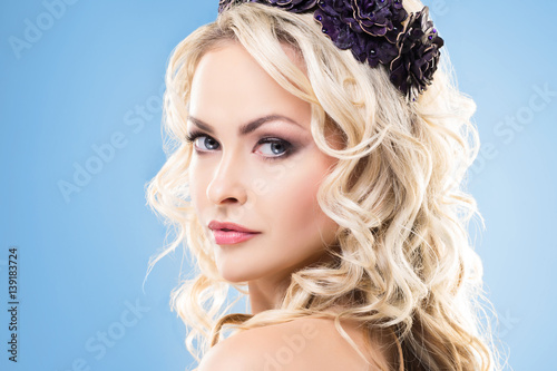 Beauty portrait of attractive blond girl with curly hair and a beautiful headband over blue background.