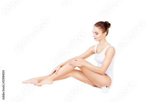 Fit and sporty girl in bodysuit isolated on white. Beautiful and healthy woman adding a cream on her legs. Sport, fitness, diet, weight loss and healthcare concept.