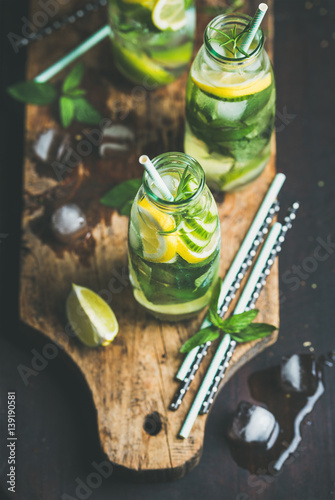 Citrus fruit and herbs infused sassi water for detox, healthy eating, dieting in glass bottles on wooden board over dark background, selective focus. Clean eating, healthy lifestyle concept