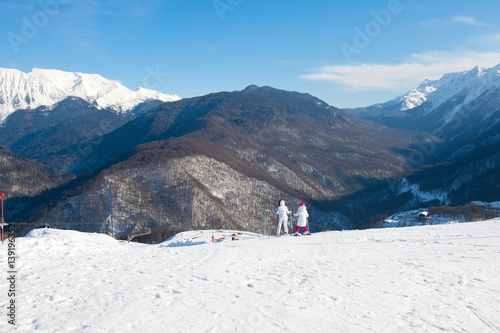 Beautiful view from the peak of snowy mountain. Tourists ride with ski on winter vacation.