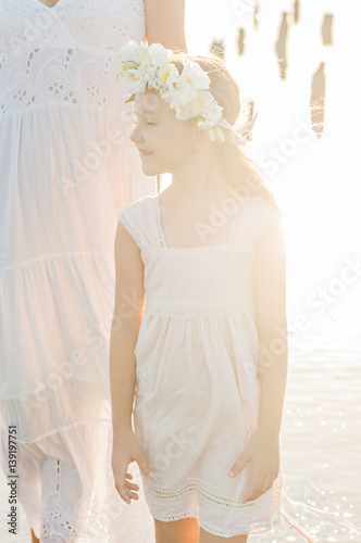 The girl in a white dress in a wreath on a head of white flowers at sunset