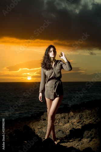 Pretty girl on rocky shore at sea during idyllic sunset