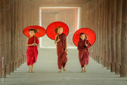 Myanmar The three novice walking on the pagoda and holding red umbrella in Mandalay,Myanmar.
