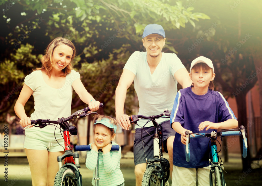 Obraz premium happy family of four with bicycles and scooter