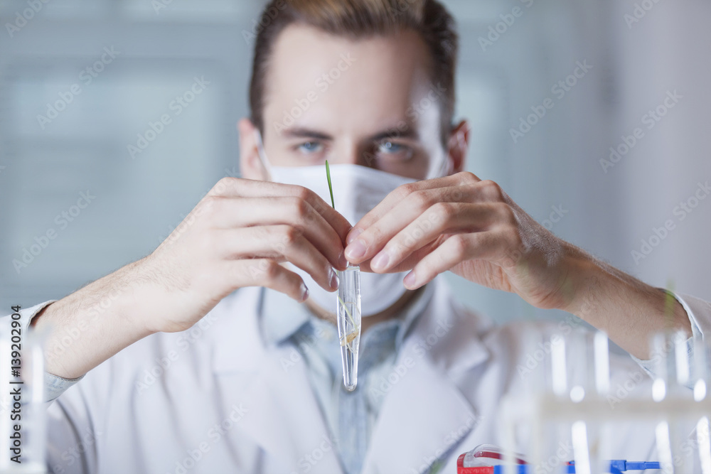 the vial with the plant in front of the face of the scientist