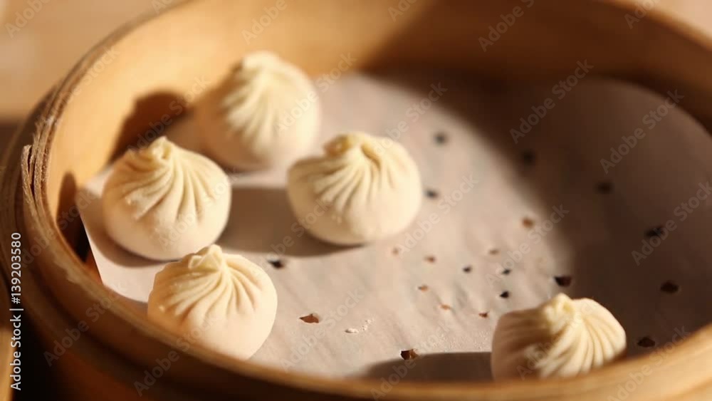 A person is placing a dumpling together with others in a bamboo steamer. He uses a bamboo steamer basket to place it on a pot of boiling water.