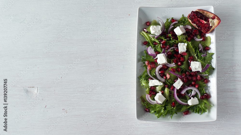 Fresh spring salad with feta cheese, red onion and pomegranate seeds in white dish. Top view, copy space Fresh spring salad with feta cheese, red onion and pomegranate seeds in white dish. Top view, copy space