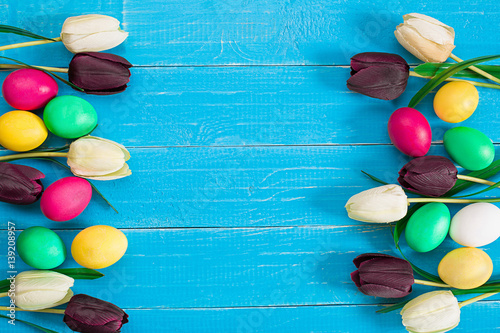 Photos colorful easter eggs and bouquet of tulips on wooden background with space for a