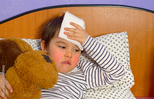 little girl with a headache in bed with teddy bear photo