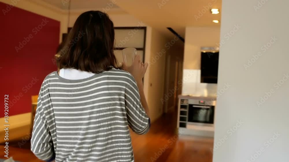 Woman drinking water and taking magazine while walking in the flat, steadycam shot
