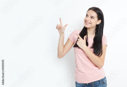 Look here. Attractive young woman pointing to space. Friendly smiling girl pointing at copyspace isolated on white background
