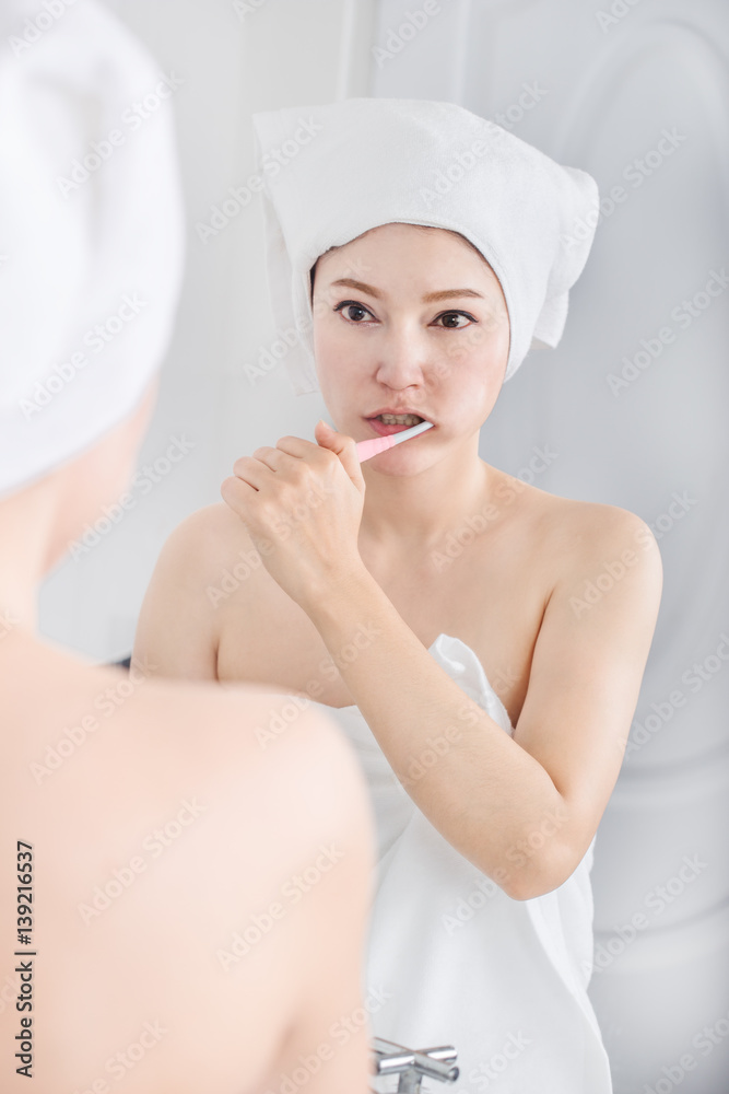 woman in bath towel brushing teeth with mirror in bathroom