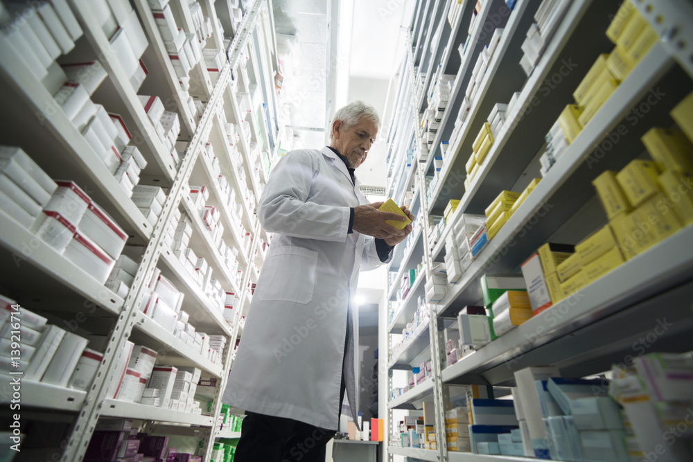 Senior Male Chemist Standing By Shelves In Pharmacy Senior Male Chemist Standing By Shelves In Pharmacy