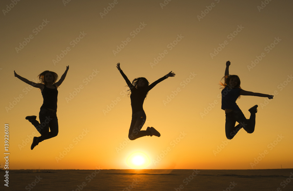 Three sporty funny happy woman are jumping in the air at sunset time