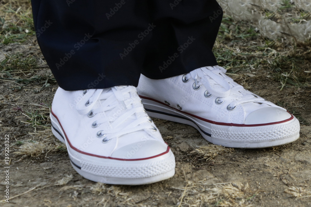 scarpe da ginnastica bianche con sopra pantalone nero su terreno sterrato