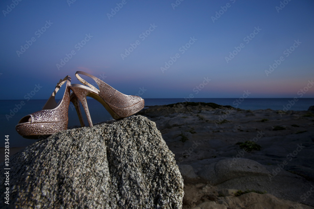 Foto Stock dettaglio di scarpe con brillantini poggiati su una roccia con  sfondo mare al tramonto | Adobe Stock